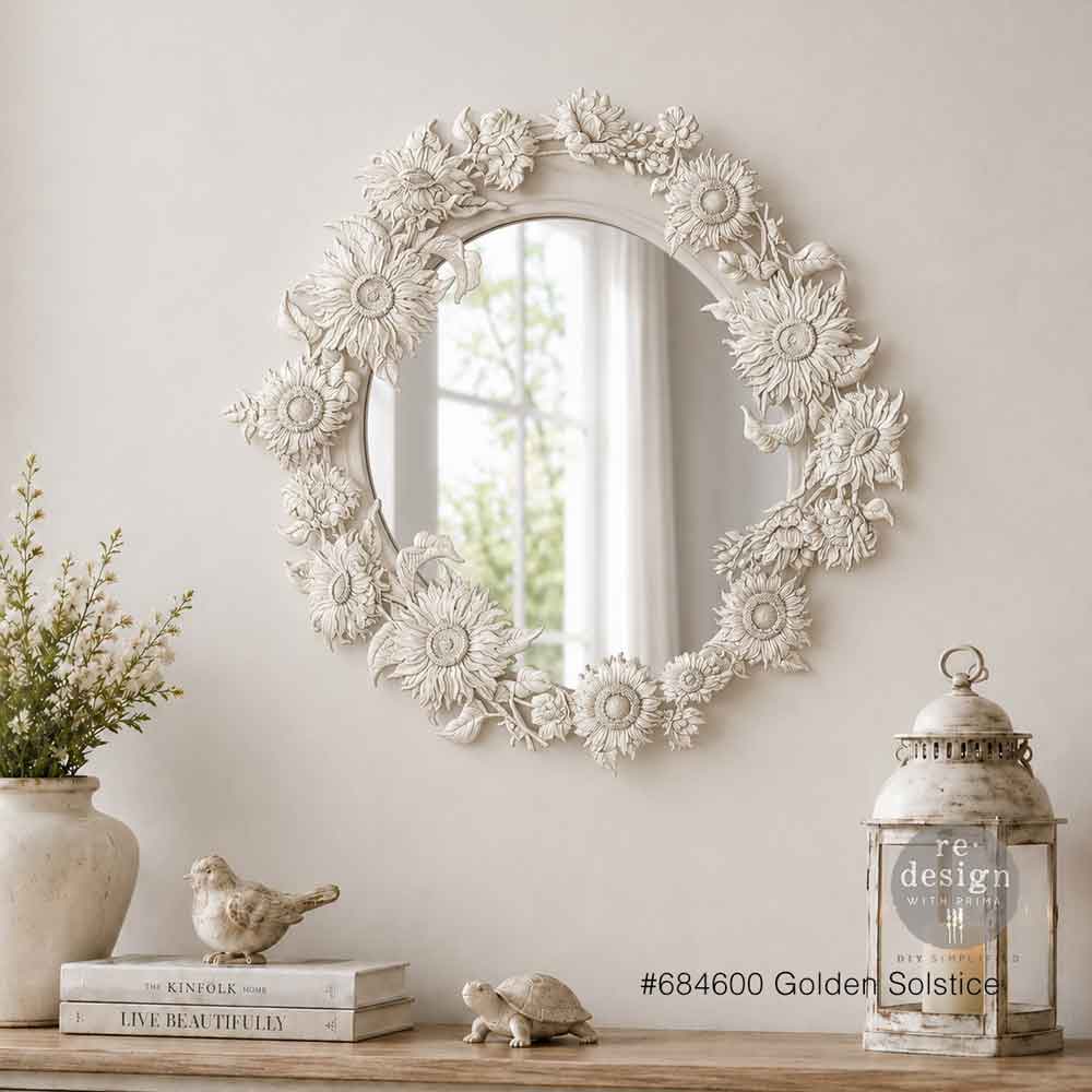 Decorative wall mirror with floral patterns on a wall with a lantern and books below.