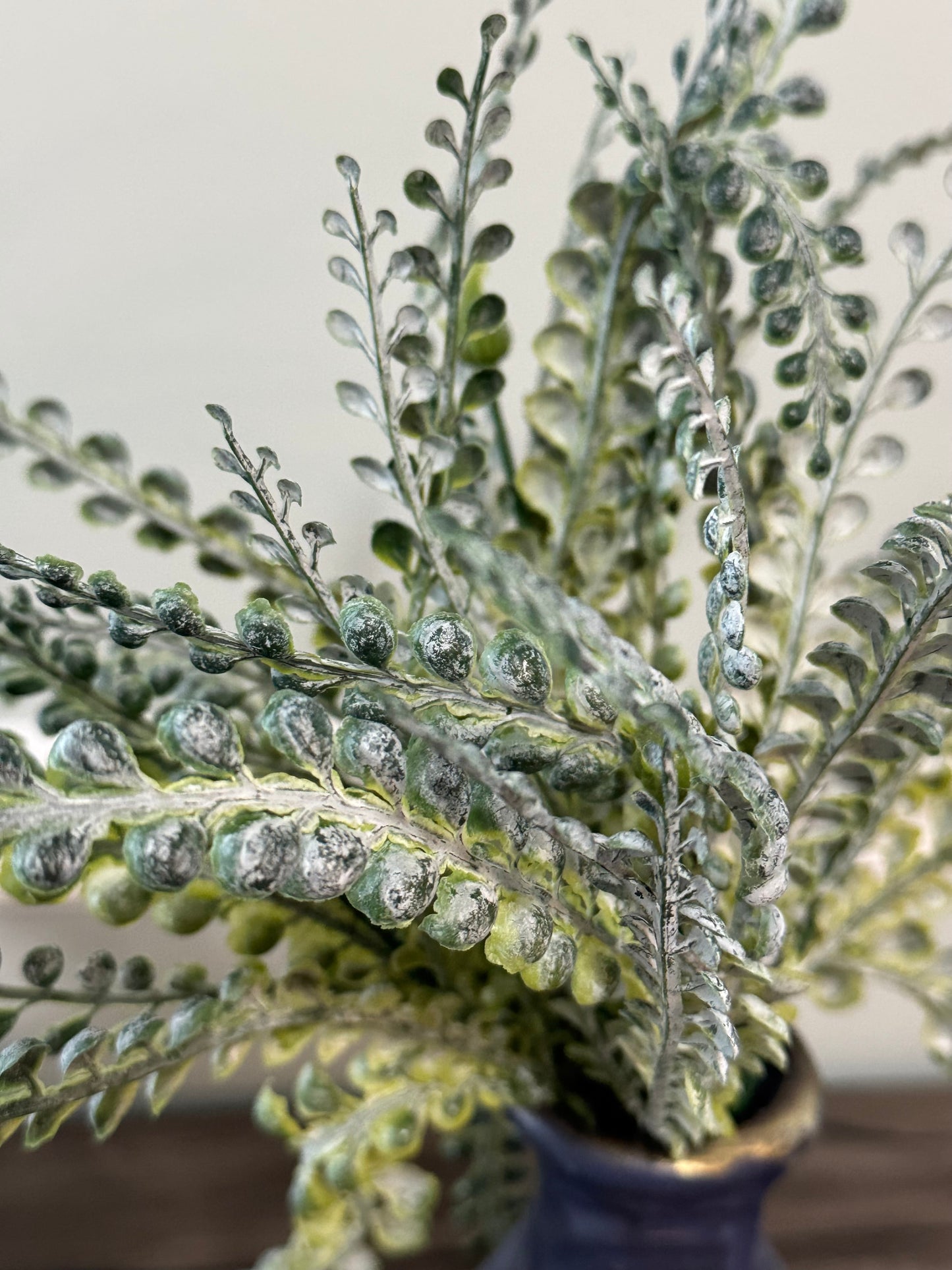 Faux fern plant with silver leaves in a pot on a neutral background