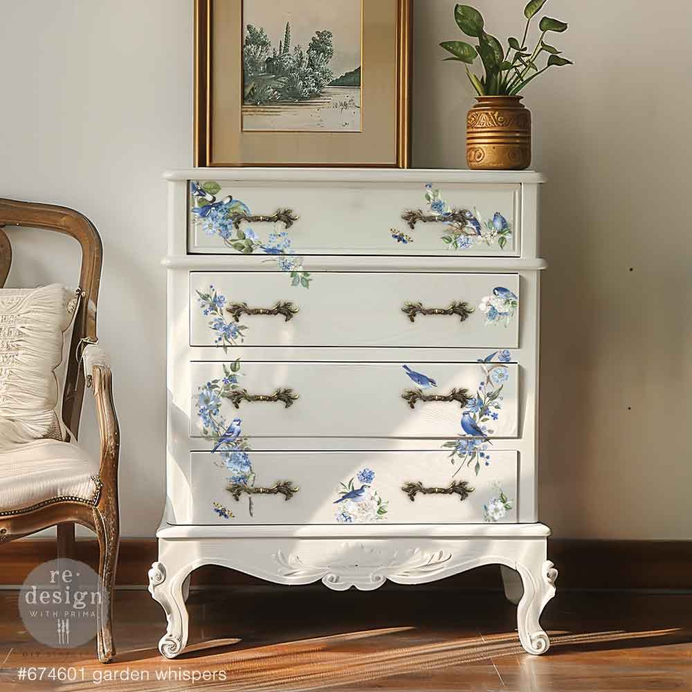 White dresser with floral decoupage design in a room with a chair and framed picture.
