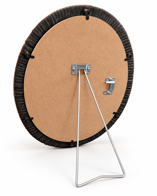Back view of a round framed picture with a brown cardboard backing, a dark textured outer rim, and a silver metal wire stand on a white background.
