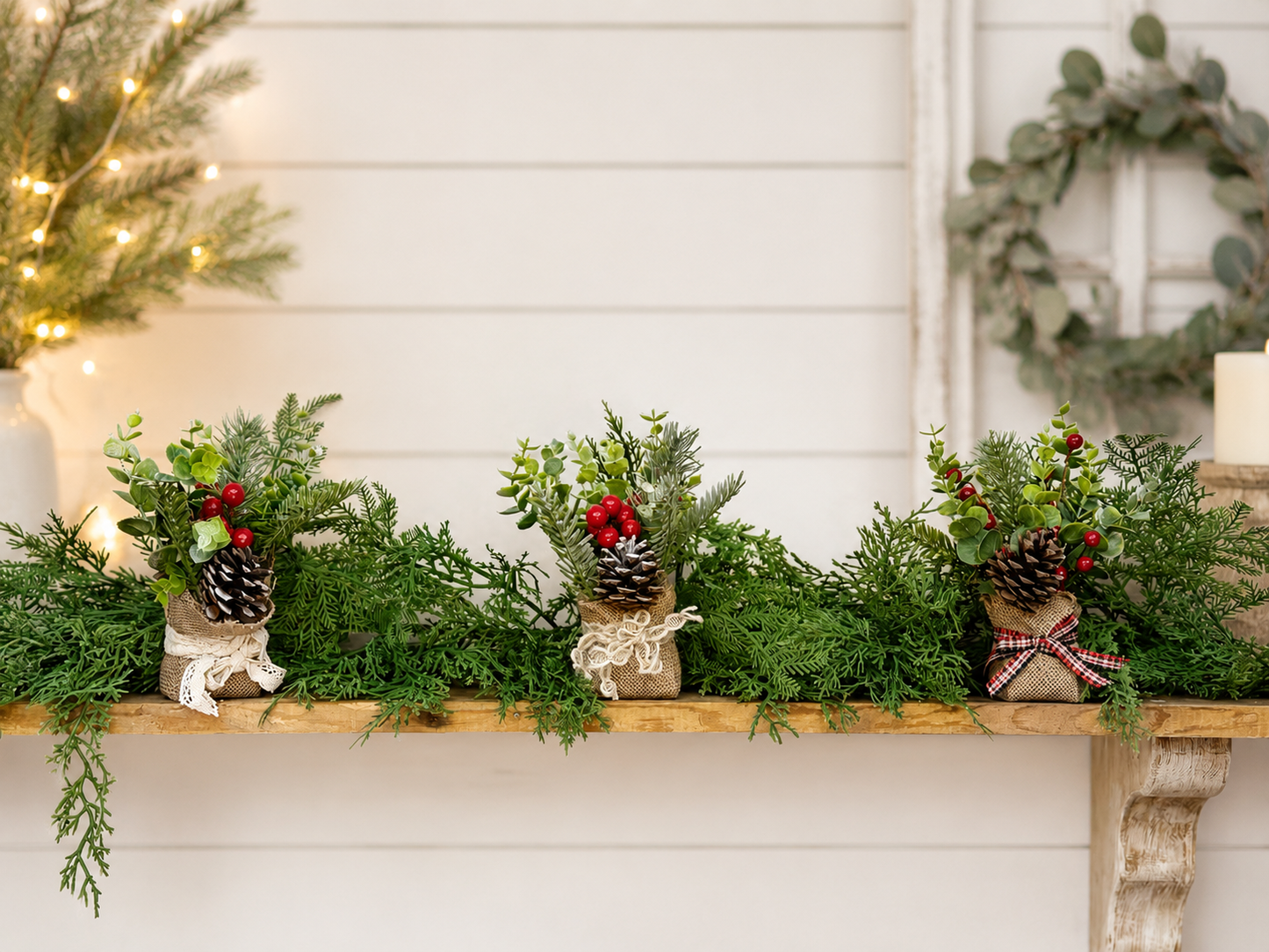 shelf green cedar garland with 3 small burlap table top arrangements with a eucalyptus wreath on the wall to the right.