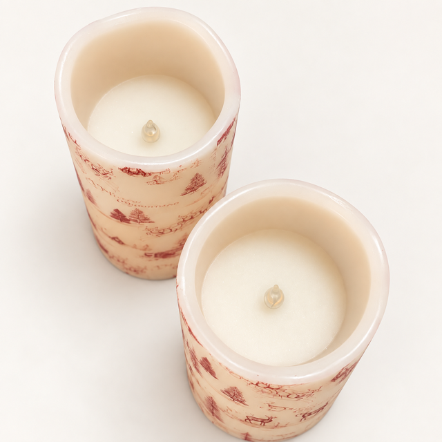 Two small pillar candles in cylindrical holders with a cream-colored wax and a beige body decorated with a delicate red floral pattern, shown on a plain white background.