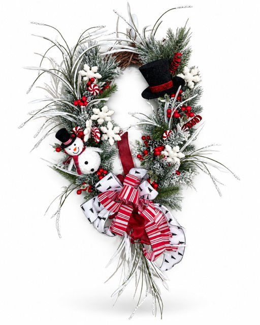 A festive Christmas wreath decorated with frosted green pine branches, white snowflakes, red berries, candy canes, a small snowman ornament, a black top hat, and a large red and white striped bow at the bottom, shown on a plain white background.
