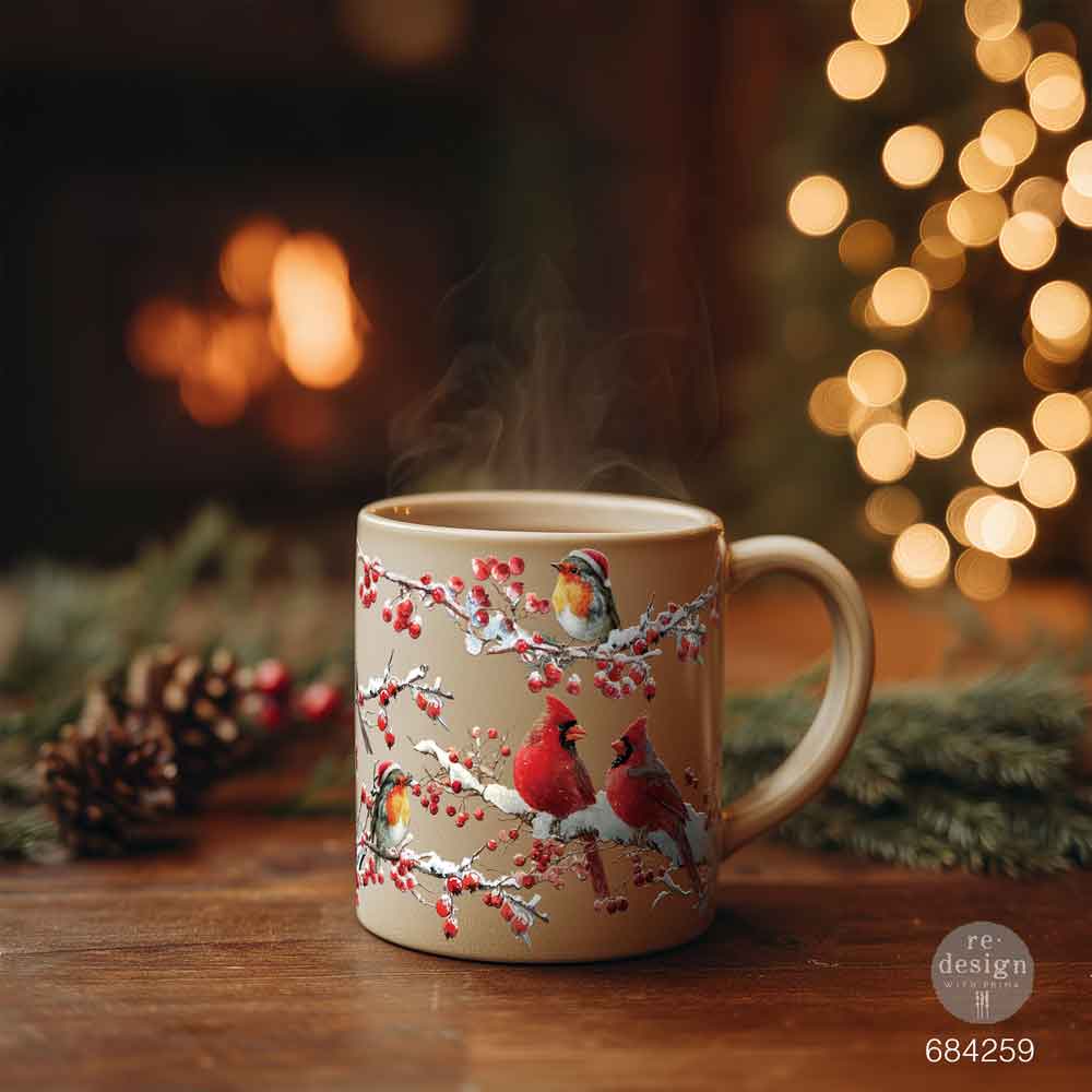 Mug with winter scene design featuring birds and berries on a wooden table with a fireplace and lights in the background.