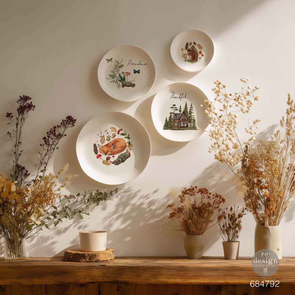 Decorative wall with plates featuring nature-themed designs, surrounded by dried plants on a wooden surface.