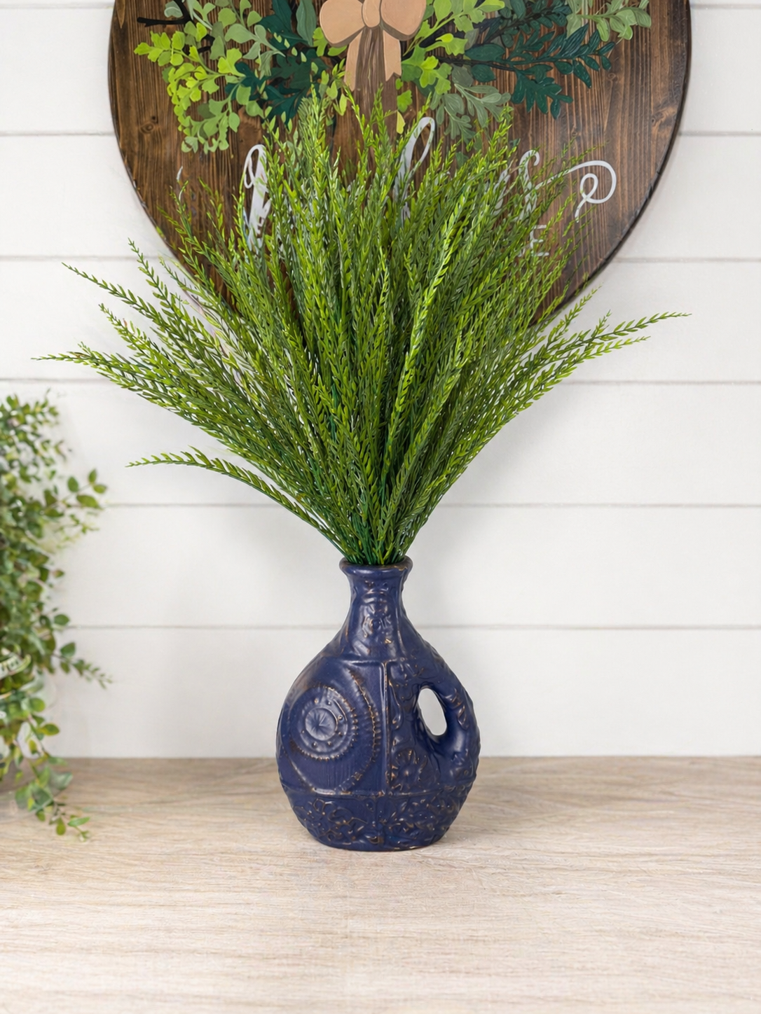 Navy blue ceramic vase with green foliage against a white wall