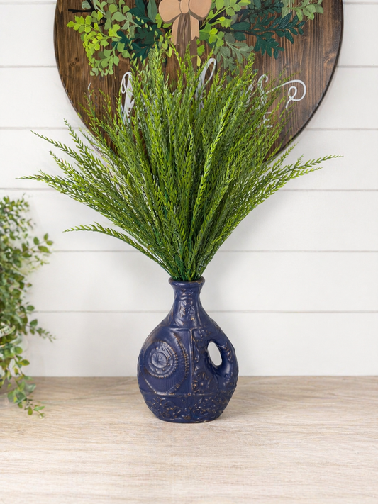 Navy blue ceramic vase with green foliage against a white wall