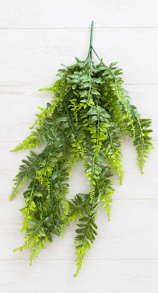 A bunch of artificial green fern branches with detailed, realistic leaves, arranged against a light-colored wooden plank background.