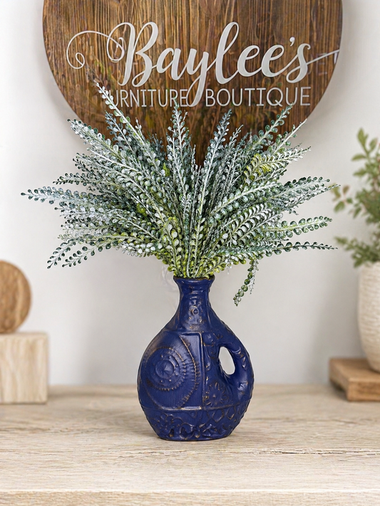 Navy blue vase with greenery on a wooden surface, with 'Baylee's Furniture Boutique' sign in the background.