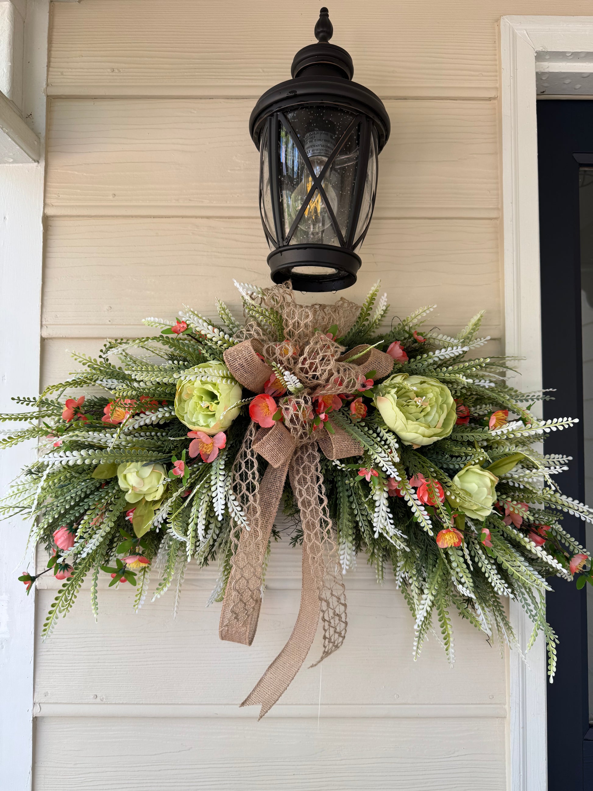 Decorative wreath with flowers and burlap ribbon hanging on a door.