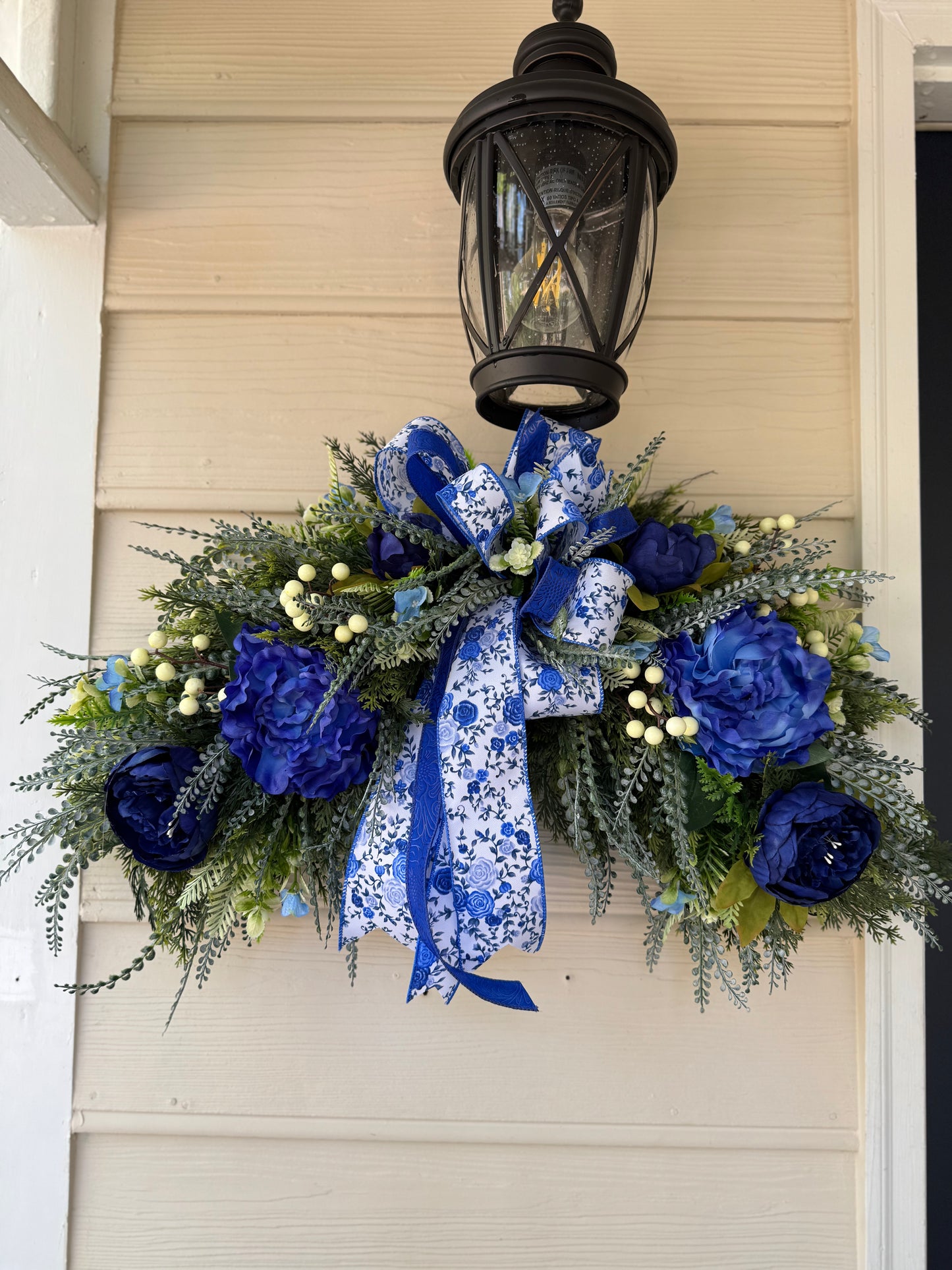 Decorative wreath with blue flowers and ribbons hanging on a door.