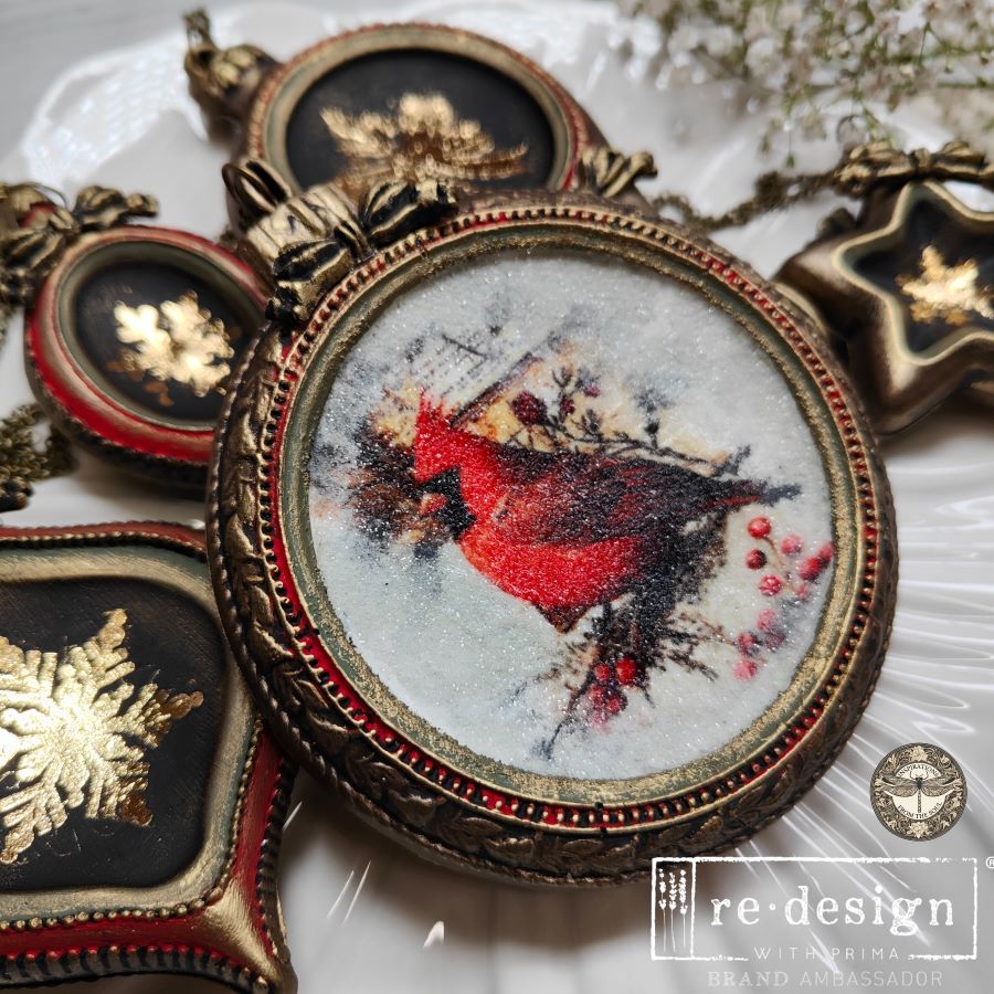 Decorative brooch with a red bird design in an ornate gold frame on a white background.