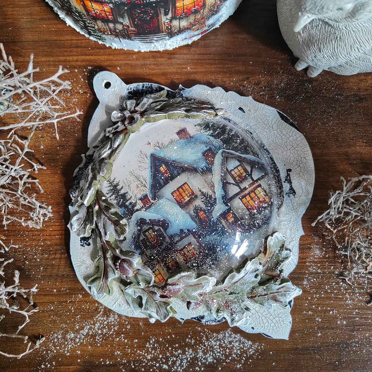 Decorative Christmas ornament with a winter scene on a wooden surface.