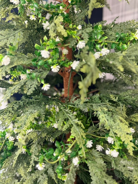 Close-up of a green artificial tree or shrub with fine needle-like foliage, small brown branches, and many tiny white flowers.