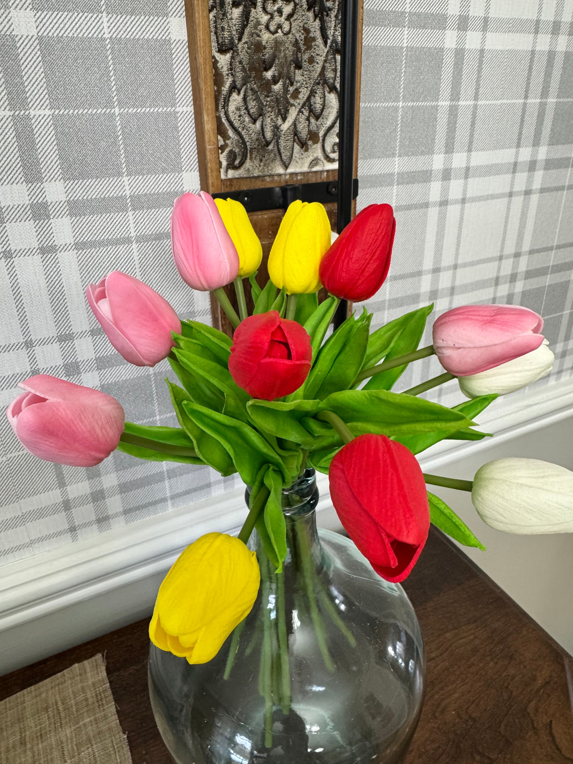 Bouquet of red, yellow, and pink tulips in a clear glass vase on a checkered tablecloth.