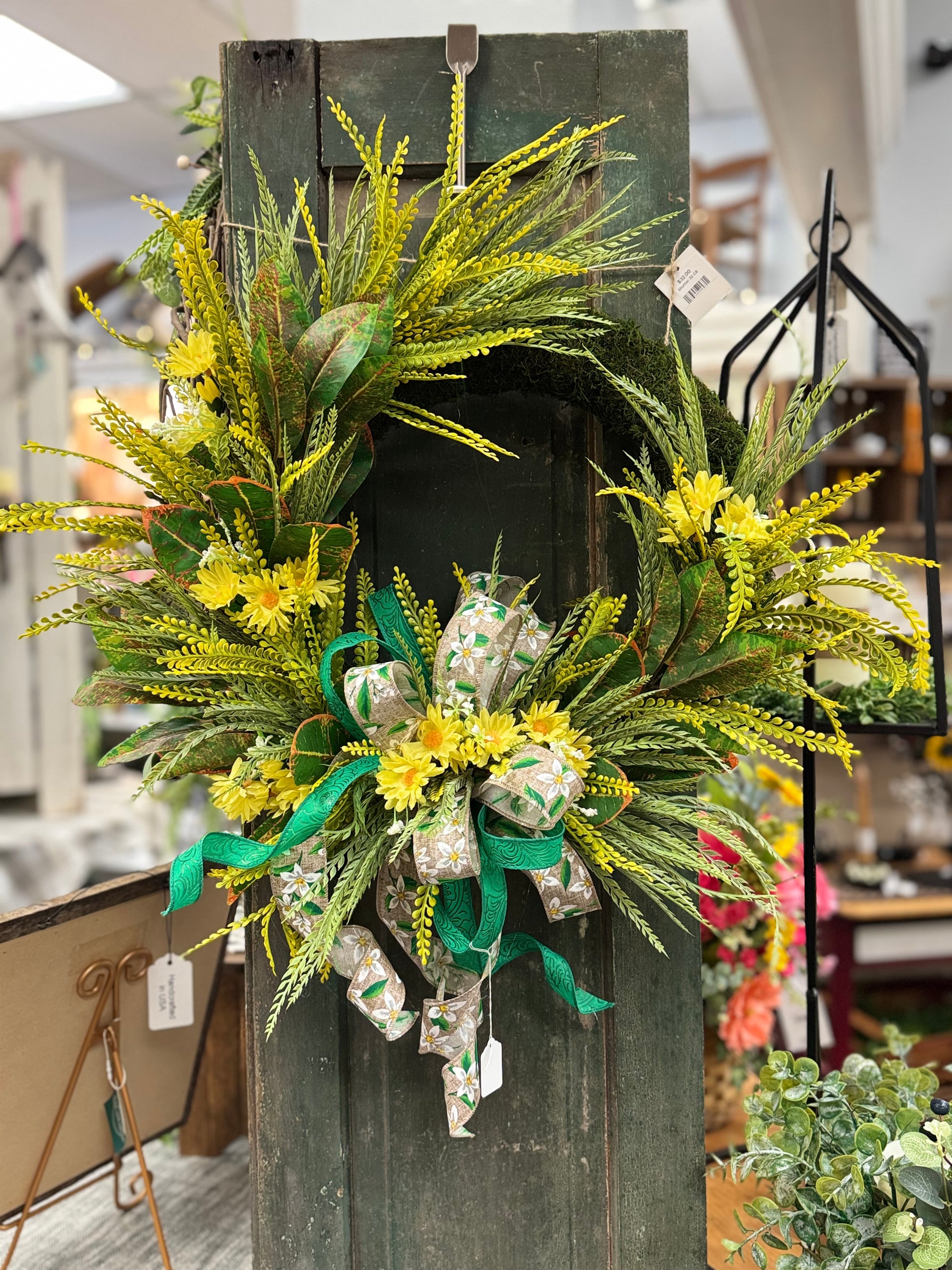 Moss wreath with yellow bead grass and greenery with a bow hanging on a door.