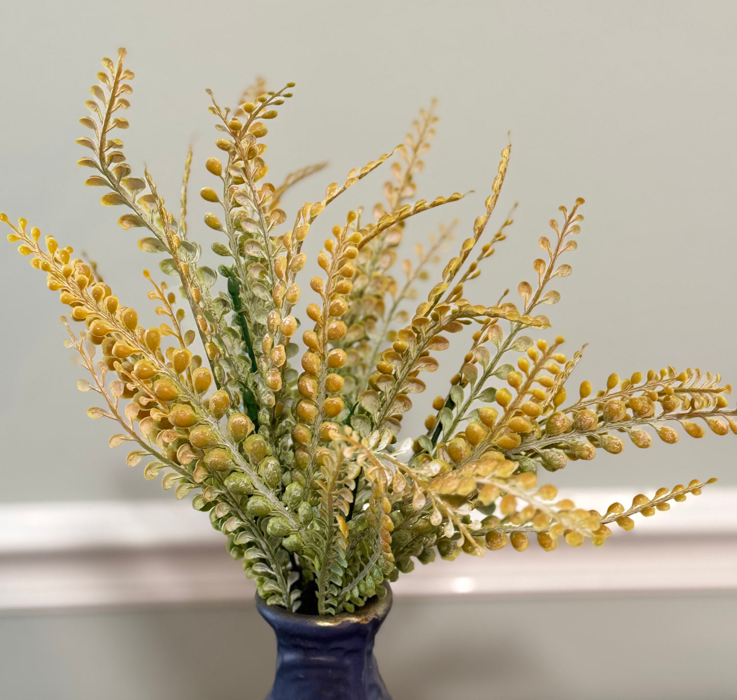 Artificial plant with yellow and green leaves in a blue vase against a neutral background