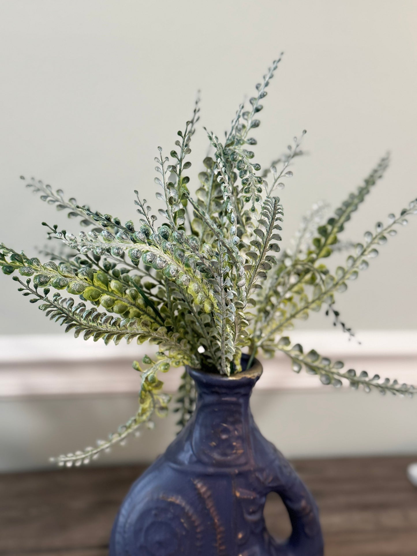 Faux plant in a blue vase on a wooden surface with a neutral background