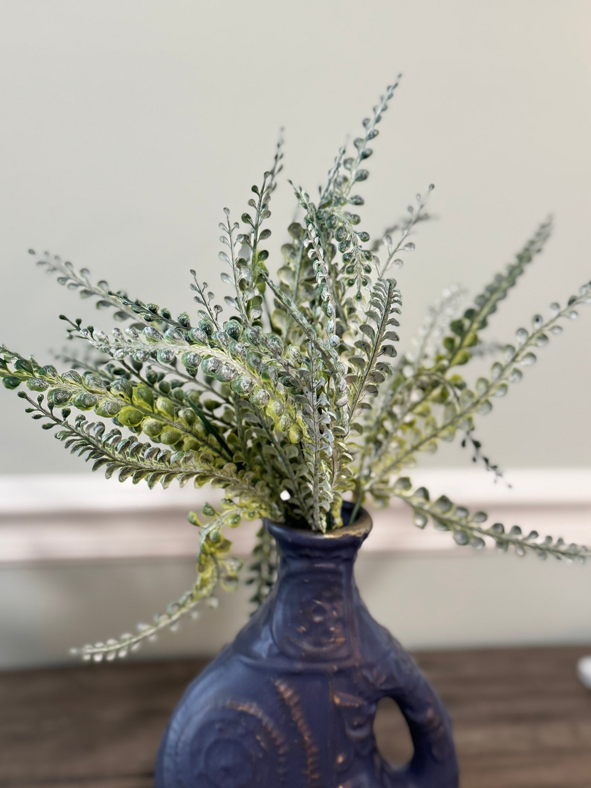 Faux plant in a blue vase on a wooden surface with a neutral background