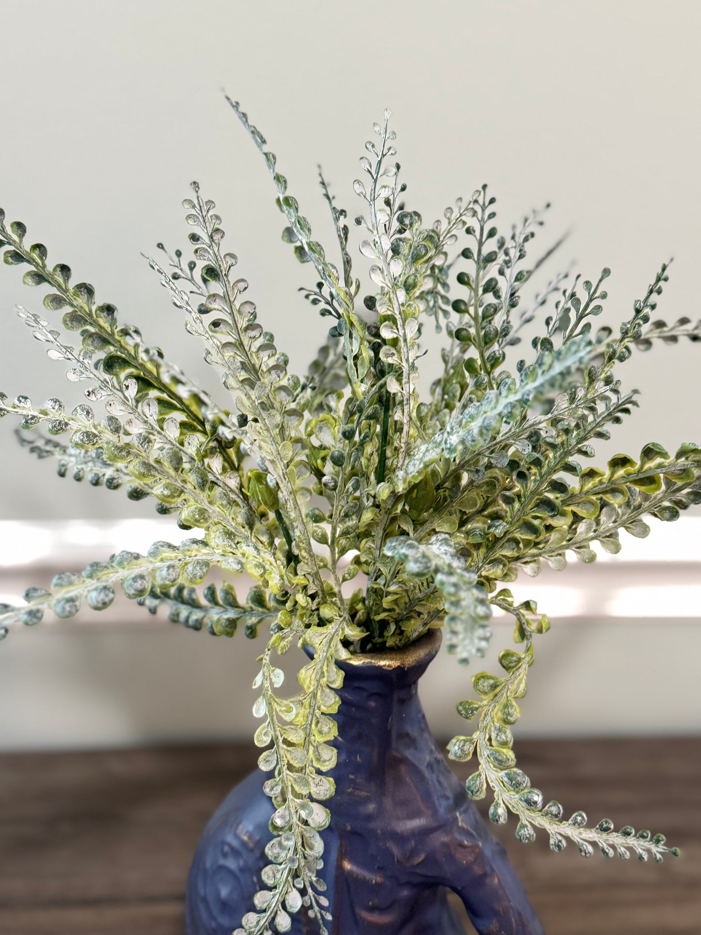 Decorative plant arrangement in a blue vase on a wooden surface with a neutral background