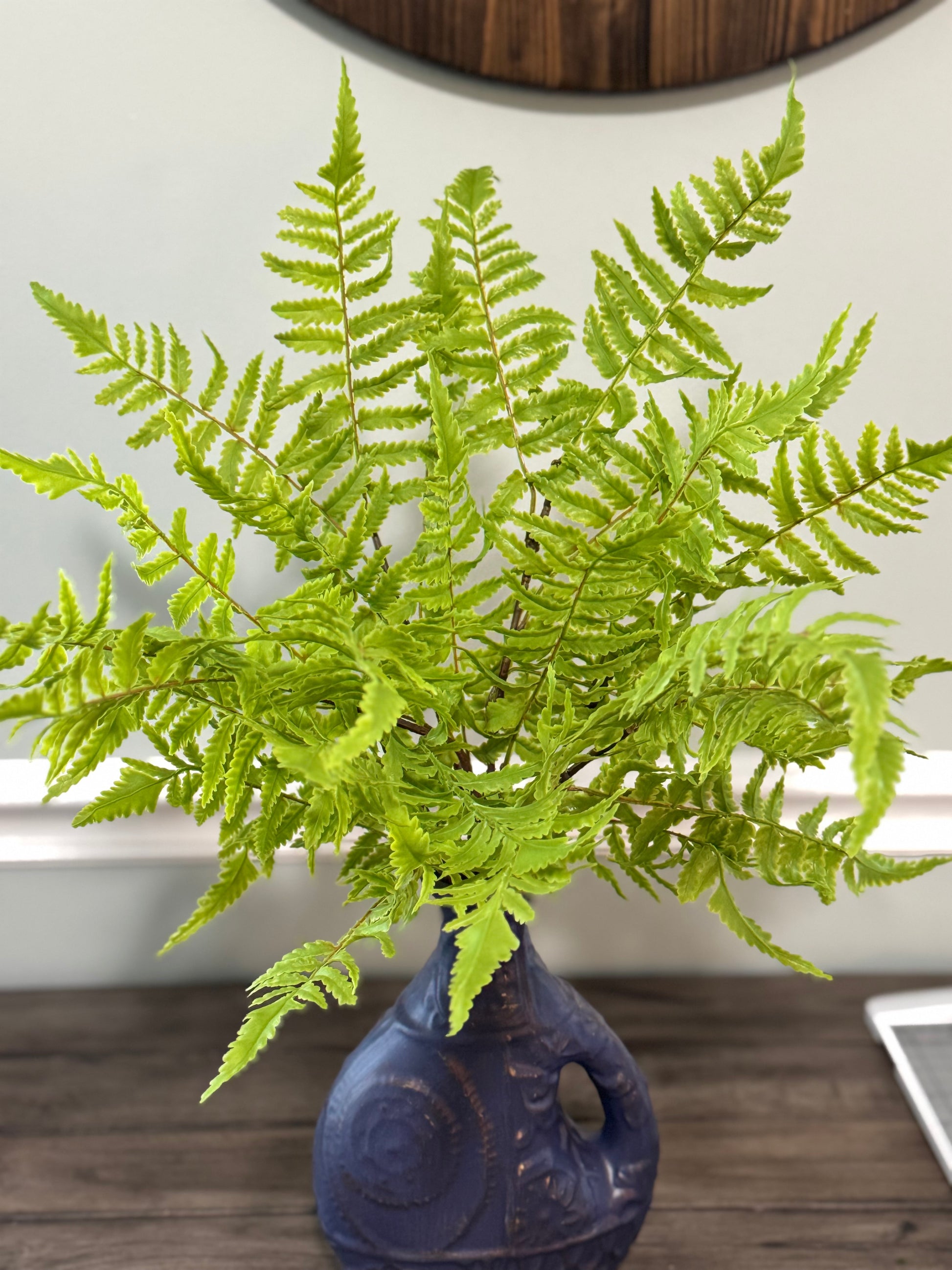 Fern plant in a blue vase on a wooden surface with a neutral background