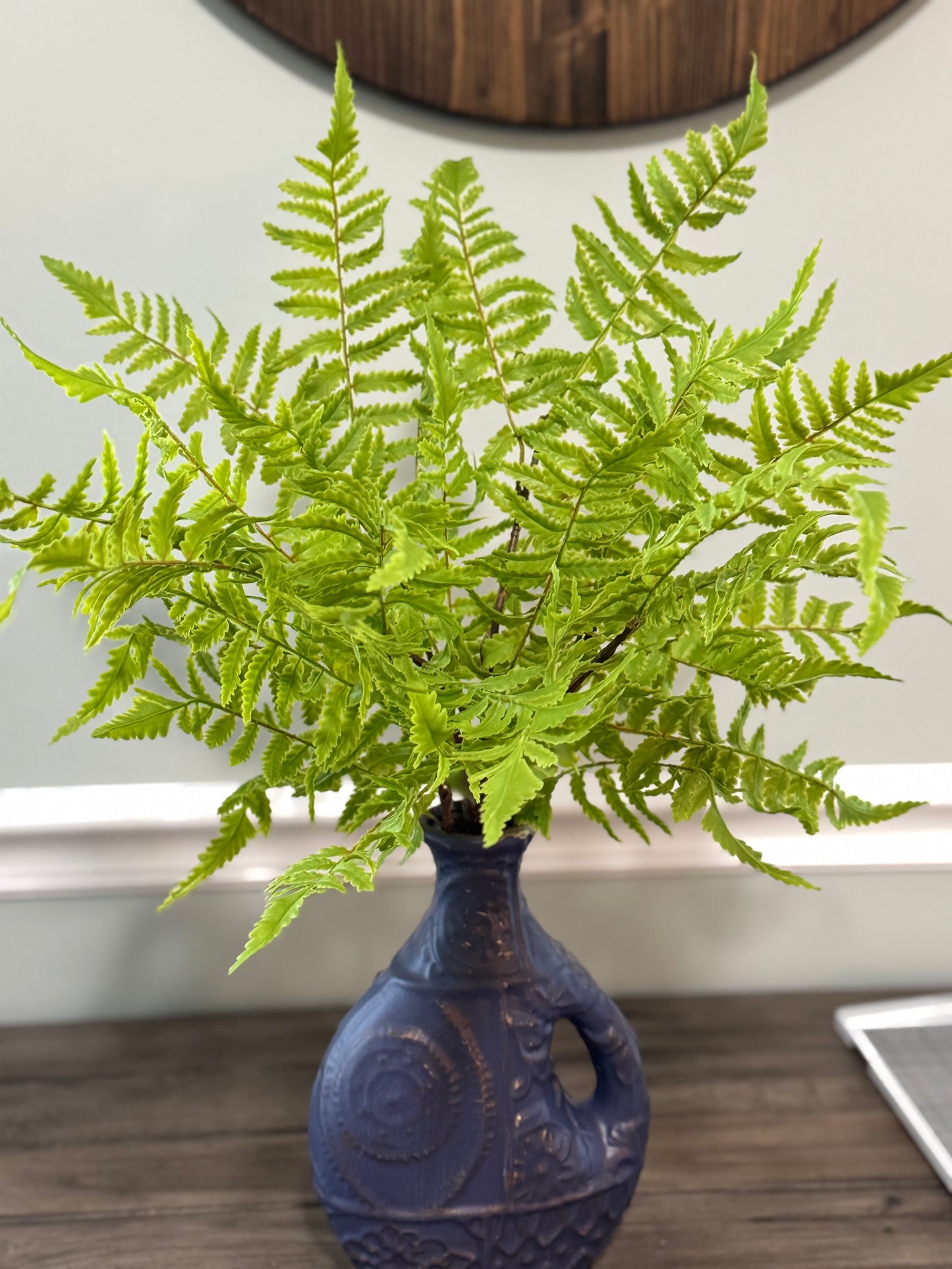 Fern in a blue vase on a wooden surface with a neutral background
