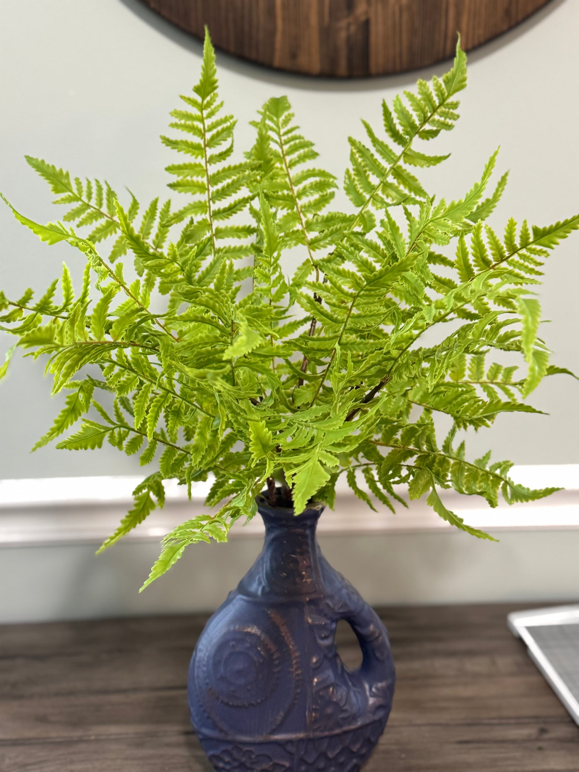 Fern in a blue vase on a wooden surface with a neutral background
