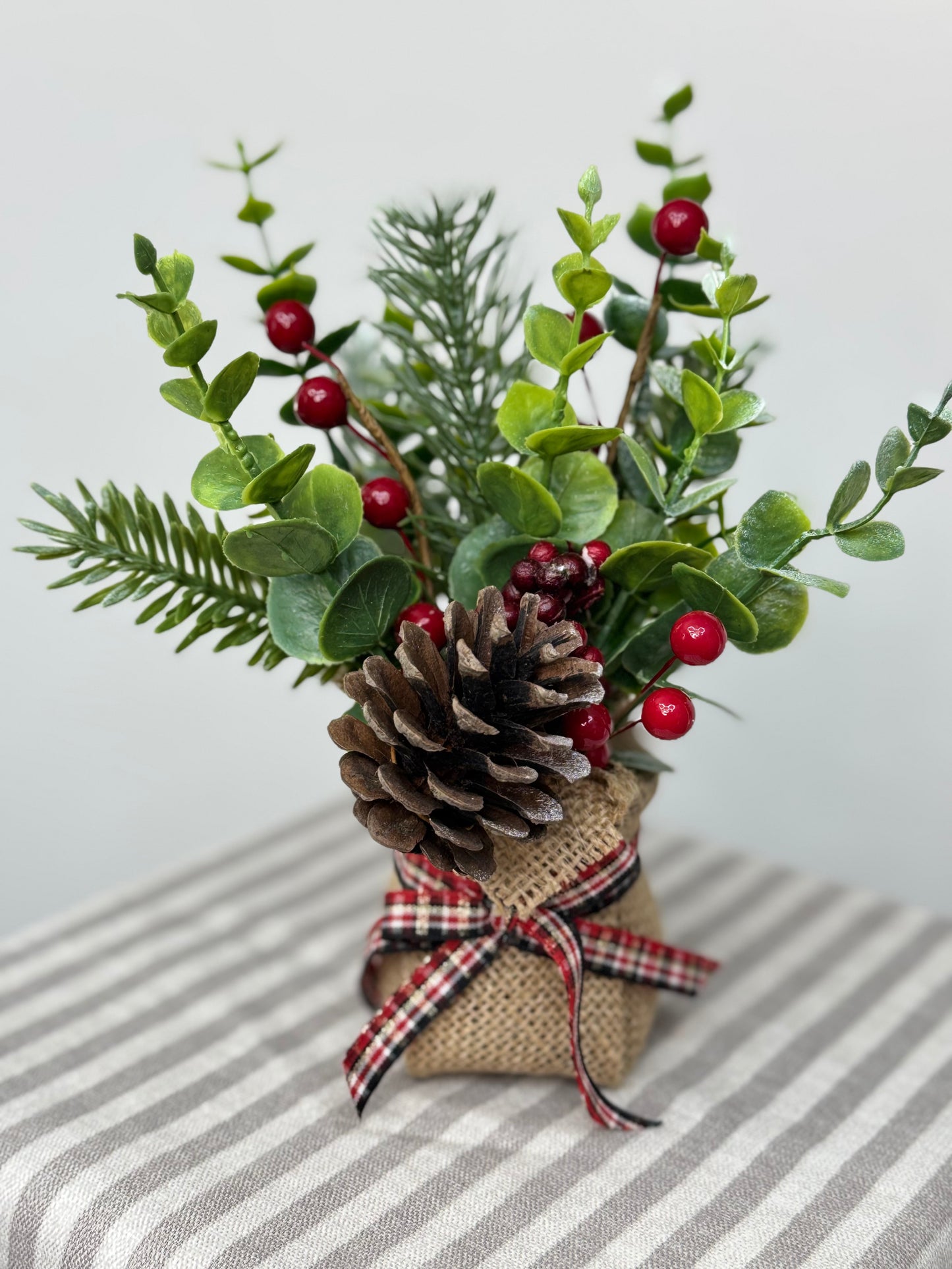 close up of small eucalyptus arrangement in a burlap base. It has pinecones, cedar, pine branches, and red berries.