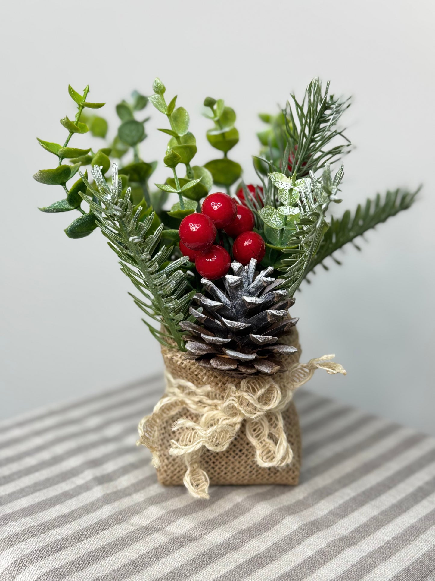 close up of small eucalyptus arrangement in a burlap base. It has pinecones, cedar, pine branches, and red berries.