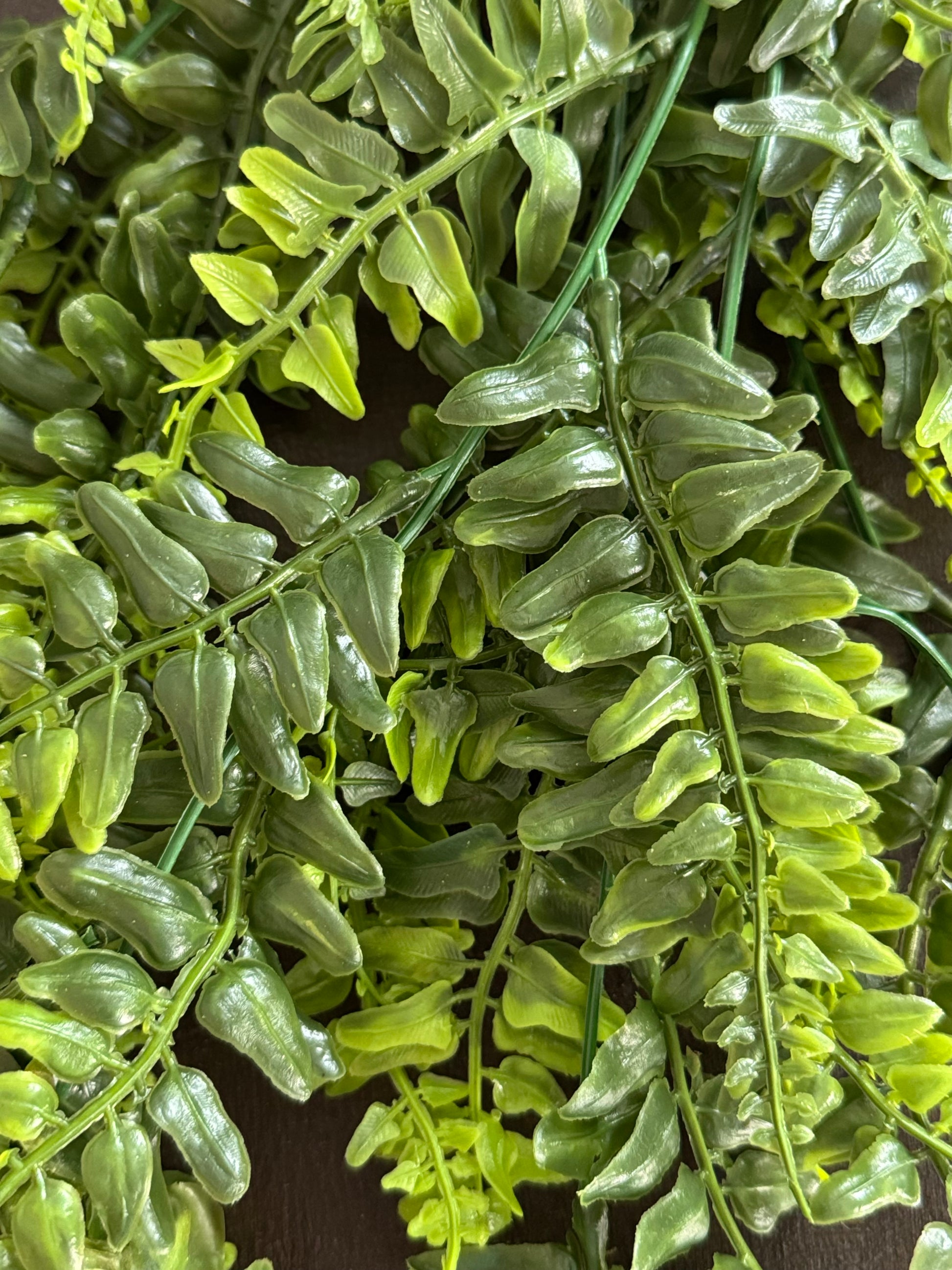 Close-up of artificial green fern-like foliage with glossy, glossy-textured leaves on branching stems.