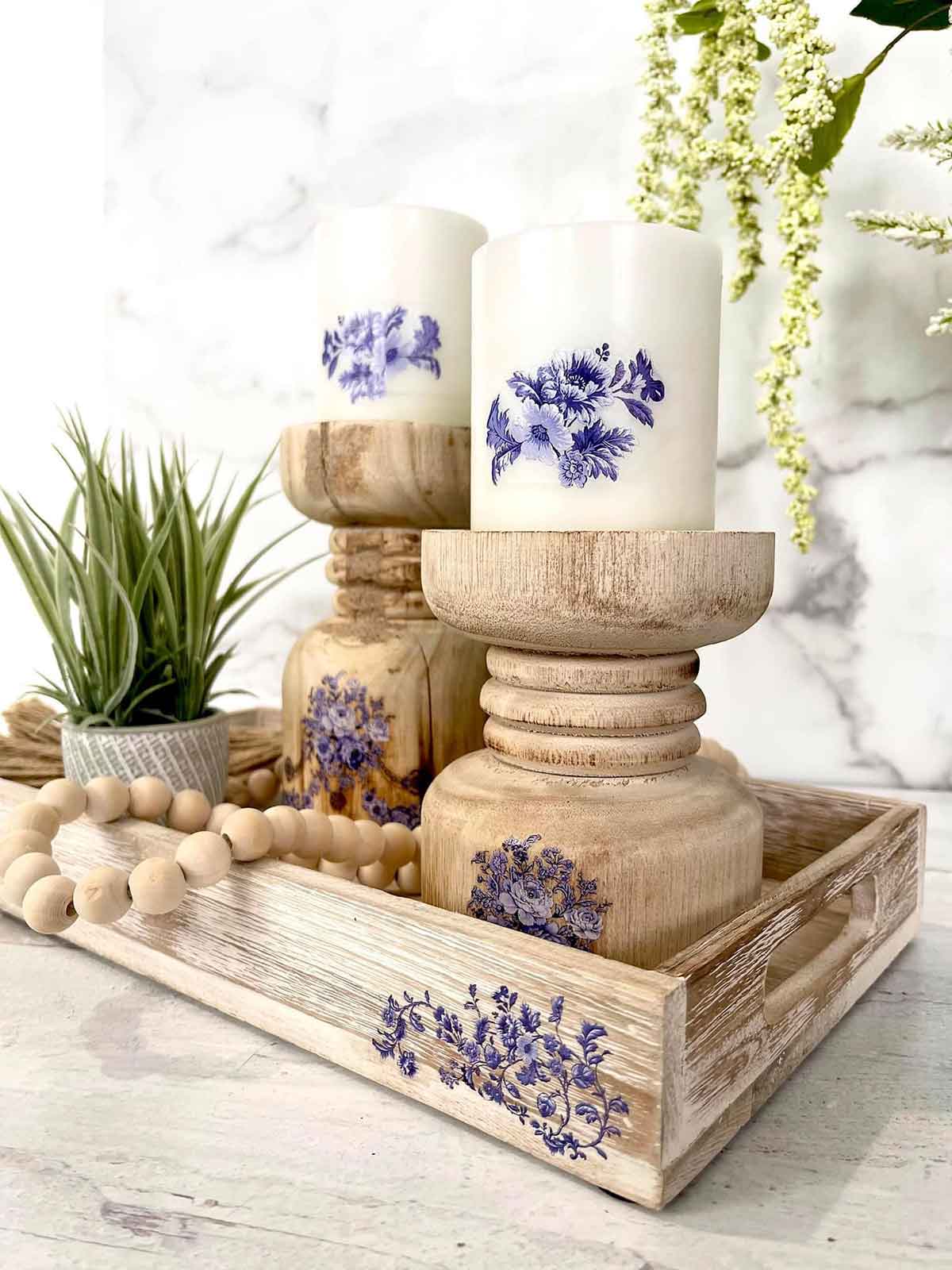 Decorative setting with wooden candle holders, candles, and a tray on a marble surface.