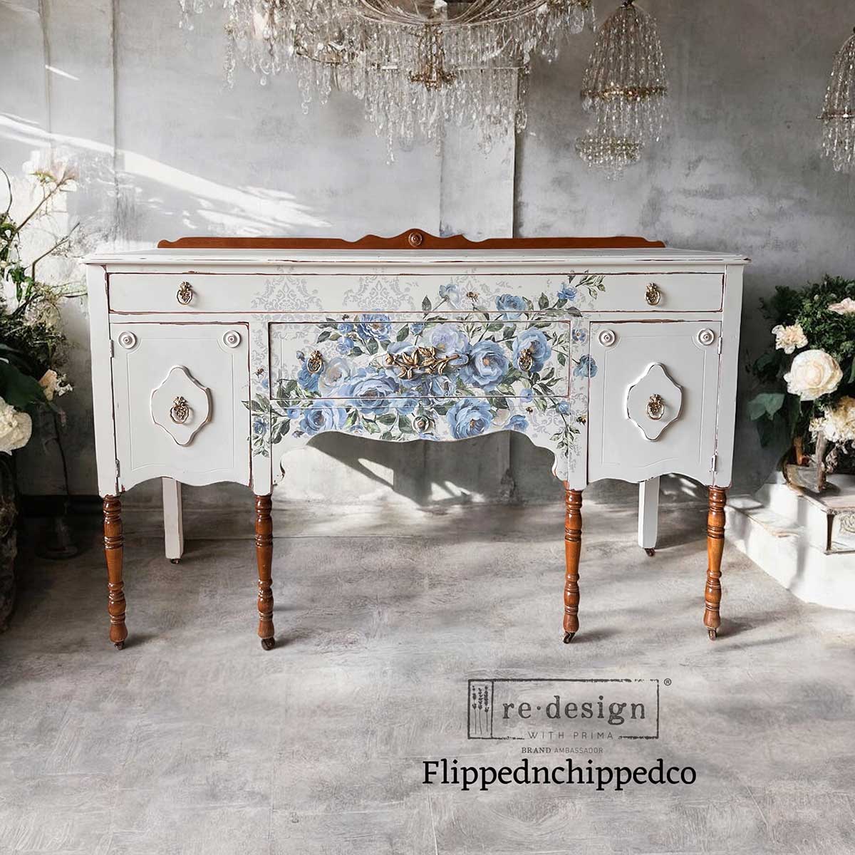 Decorative white sideboard with floral design in a room with chandeliers and flowers.