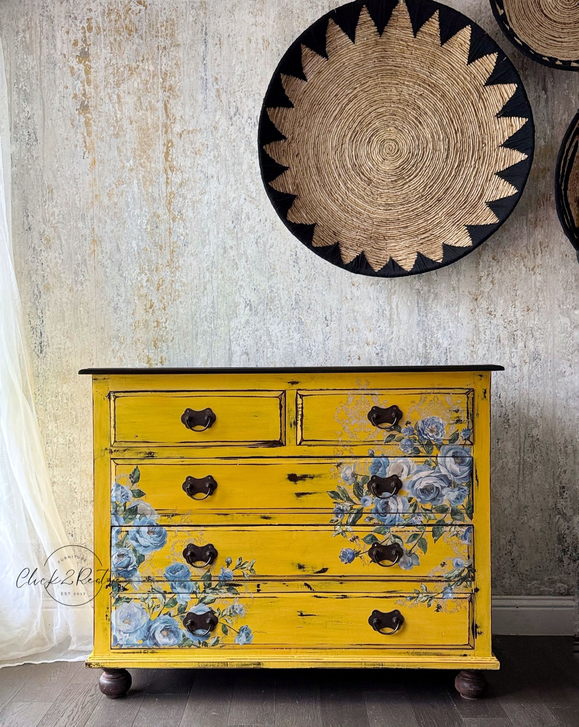 Yellow dresser with floral design against a textured wall with decorative plates.