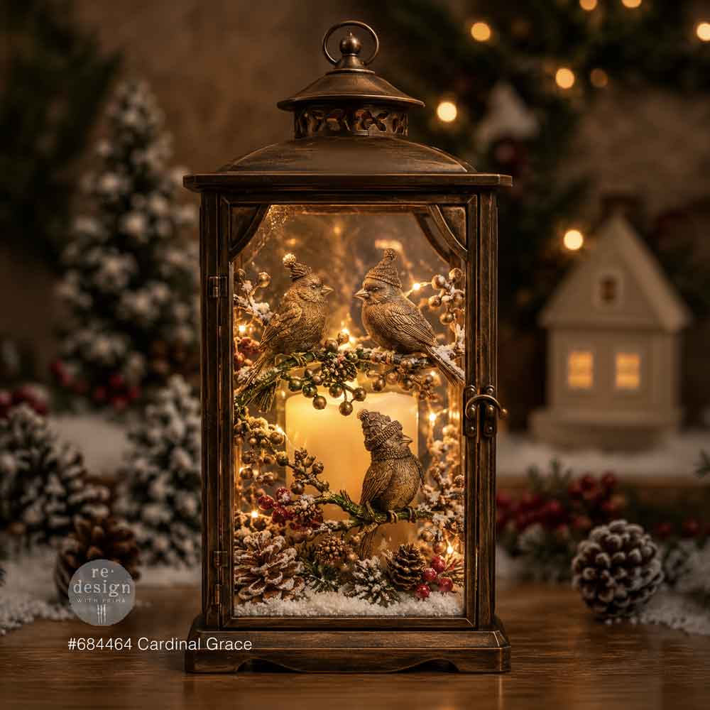 Decorative lantern with birds and winter elements on a wooden surface, blurred Christmas tree and lights in the background.