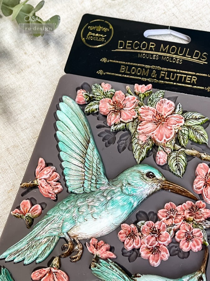 a close up of the humming bird castings painted aqua and pink sitting on top of the silicone mould