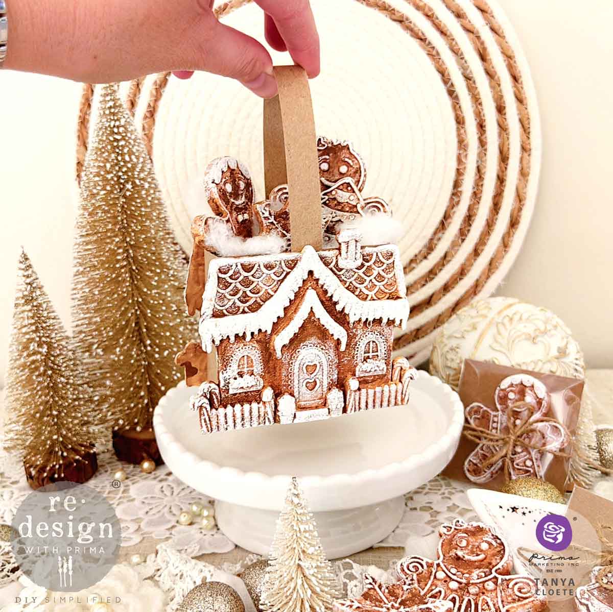 Decorative gingerbread house with a hand holding a straw, surrounded by Christmas-themed items.