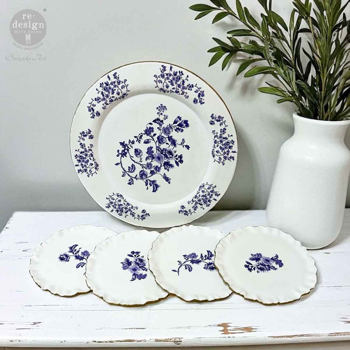 Set of white plates with blue floral patterns on a white surface with a plant in the background.