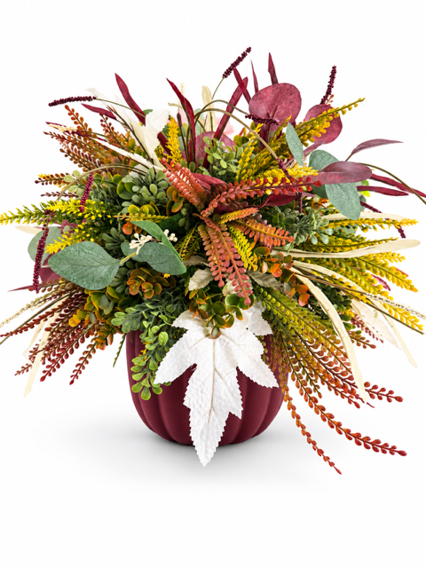 An autumn-themed floral arrangement in a dark burgundy pumpkin-shaped vase, featuring burgundy, yellow, green, and white foliage on a clean white background.