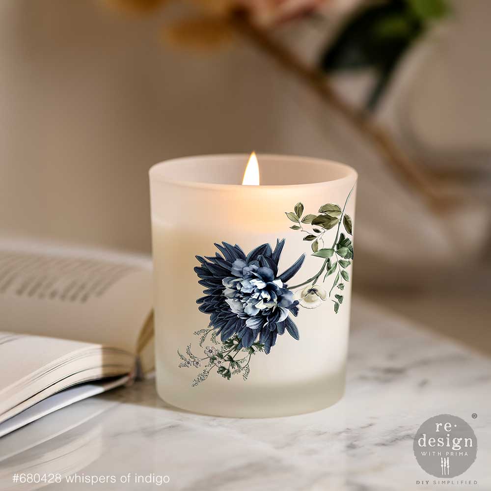 Frosted candle with floral design on a marble surface next to an open book.