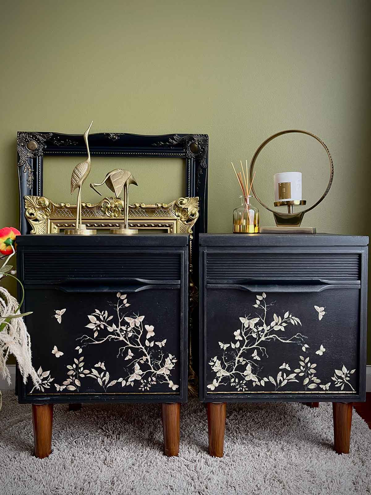 Pair of black nightstands with floral designs against a green wall.