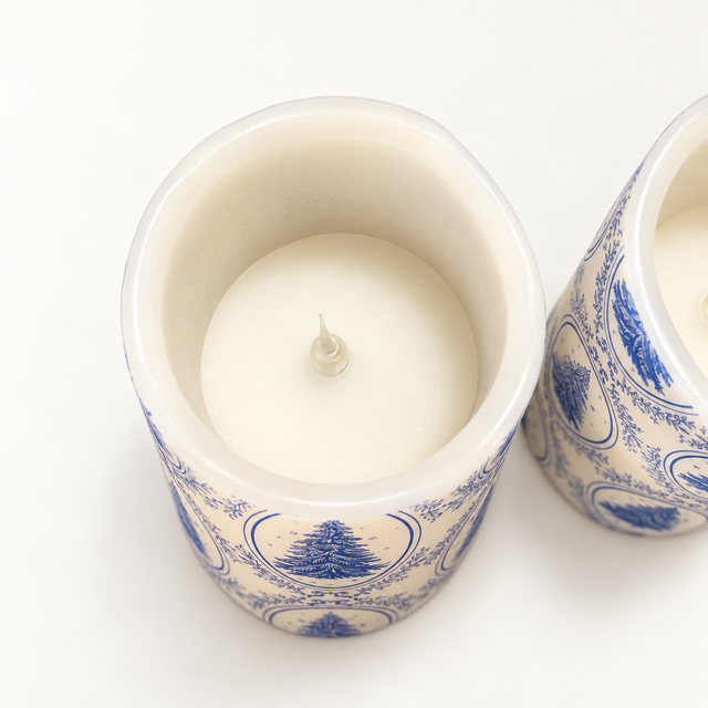 Top-down view of a white wax candle in a ceramic holder with a blue scenic pattern, next to another matching holder on a white background.